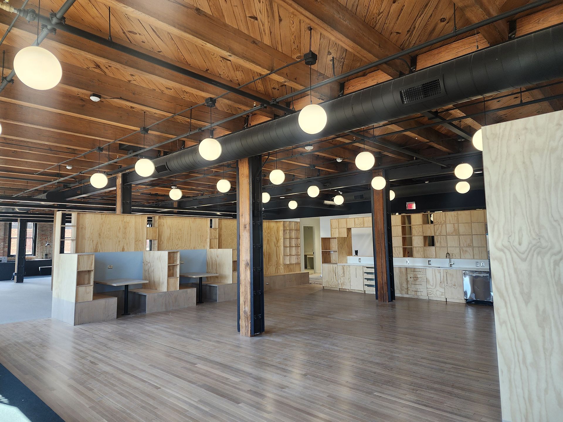 Empty industrial loft interior with exposed wood ceiling, hanging globe lights, and open seating area
