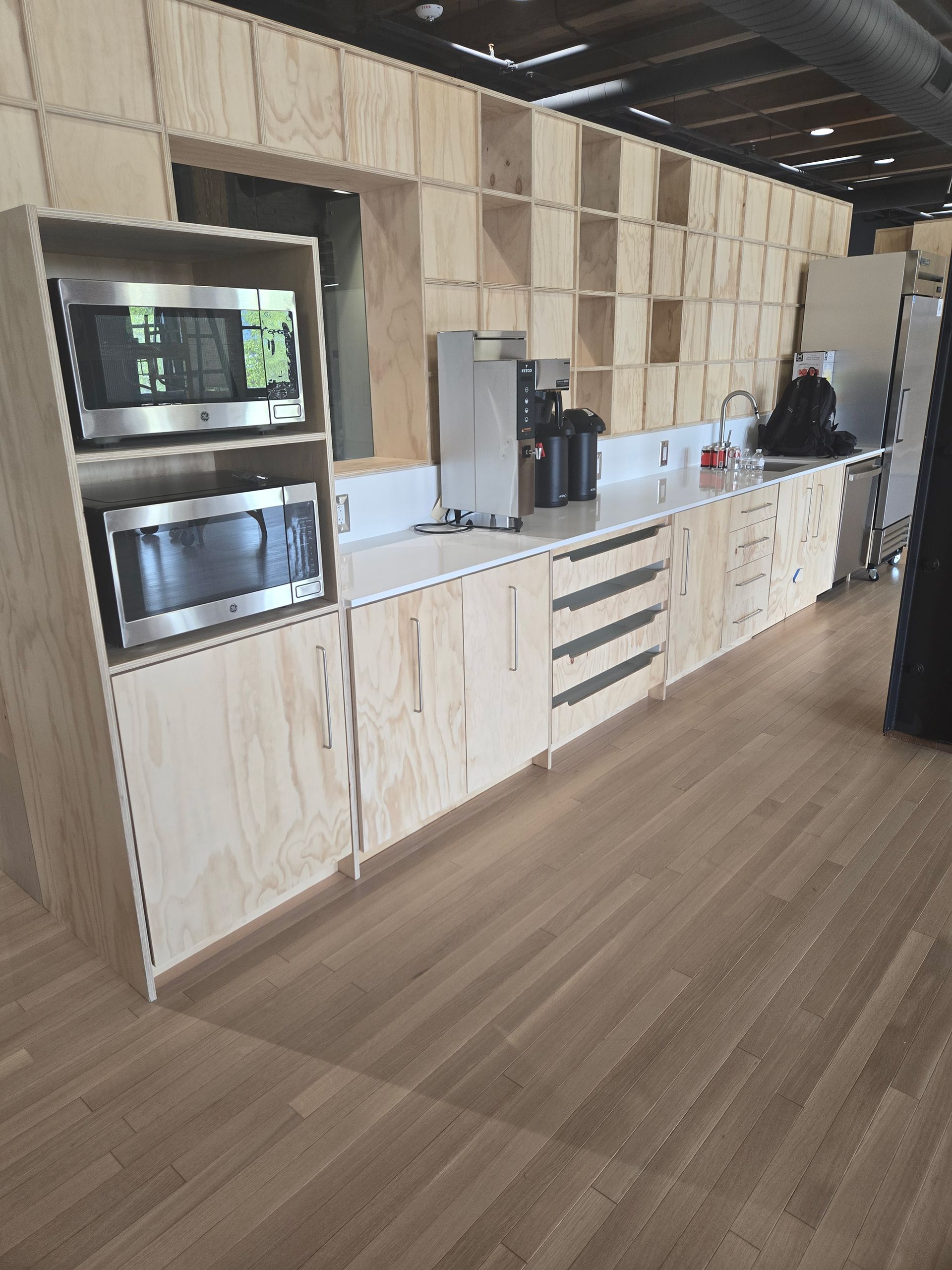 Modern kitchenette with wood cabinets, built-in microwave, coffee machine, and drawers along a wall