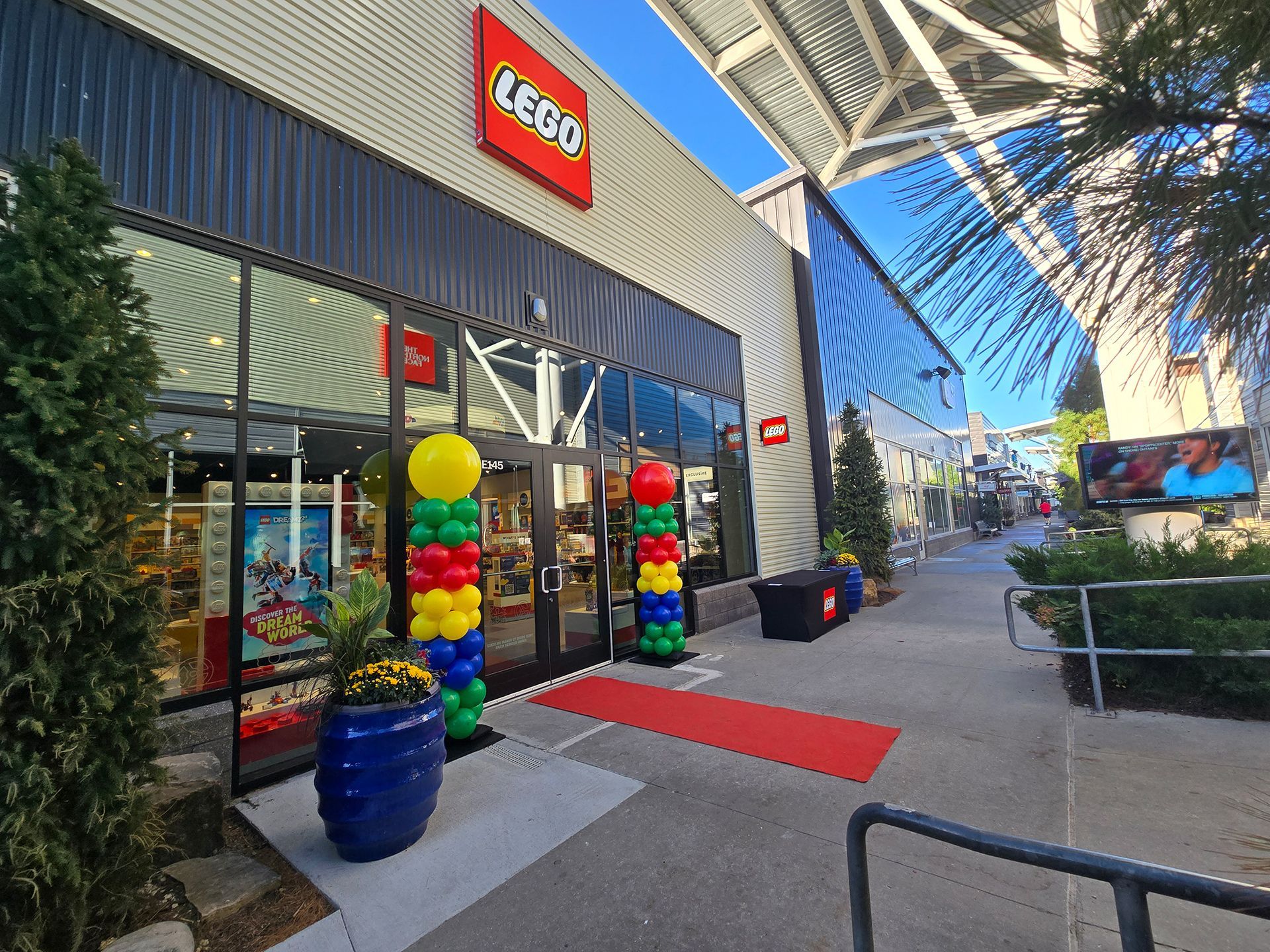 LEGO store entrance with colorful balloon columns and a red carpet on a shopping center walkway