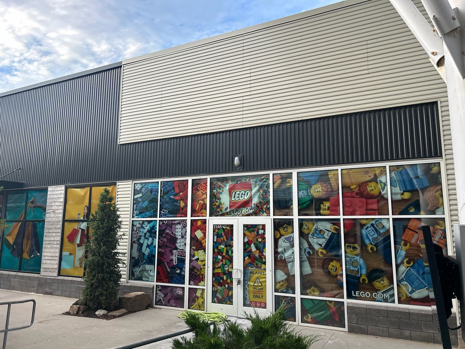 Colorful mural-covered storefront with glass doors, black siding, and a small tree in front