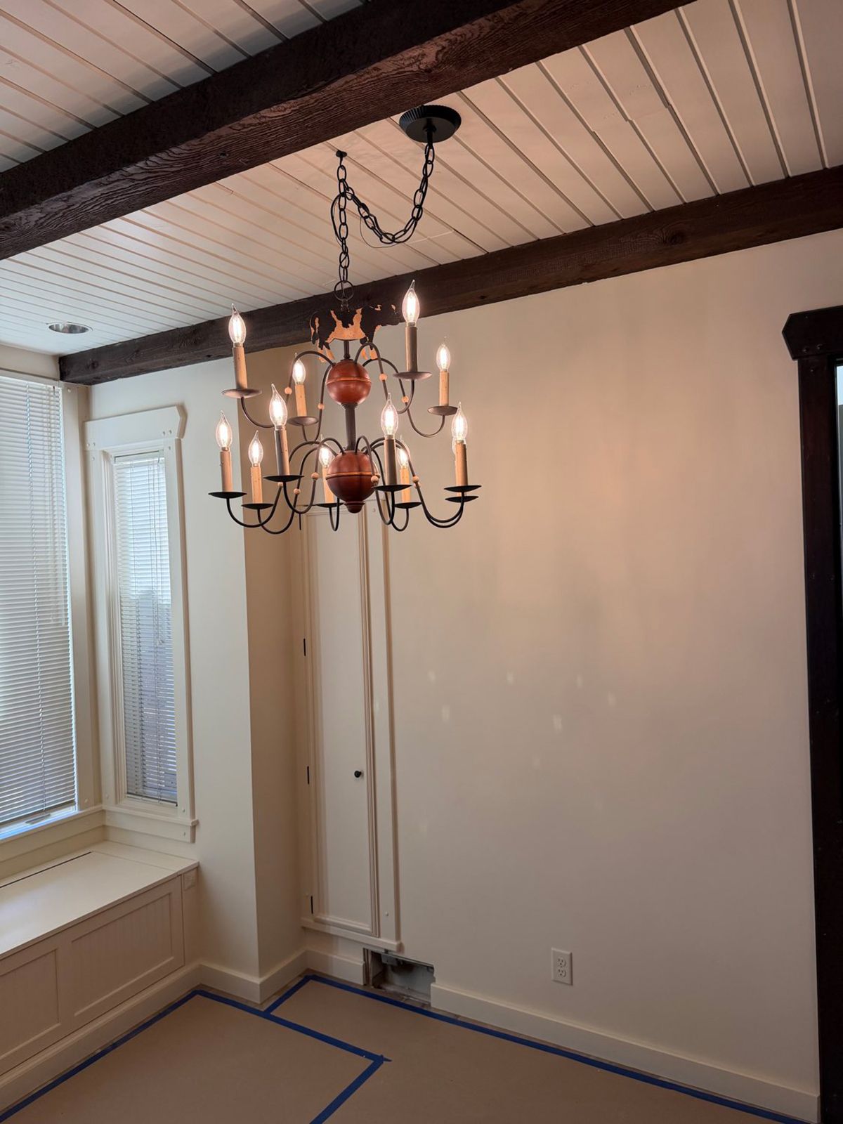 Empty dining room with hanging chandelier, white walls, and blue painter’s tape on the floor