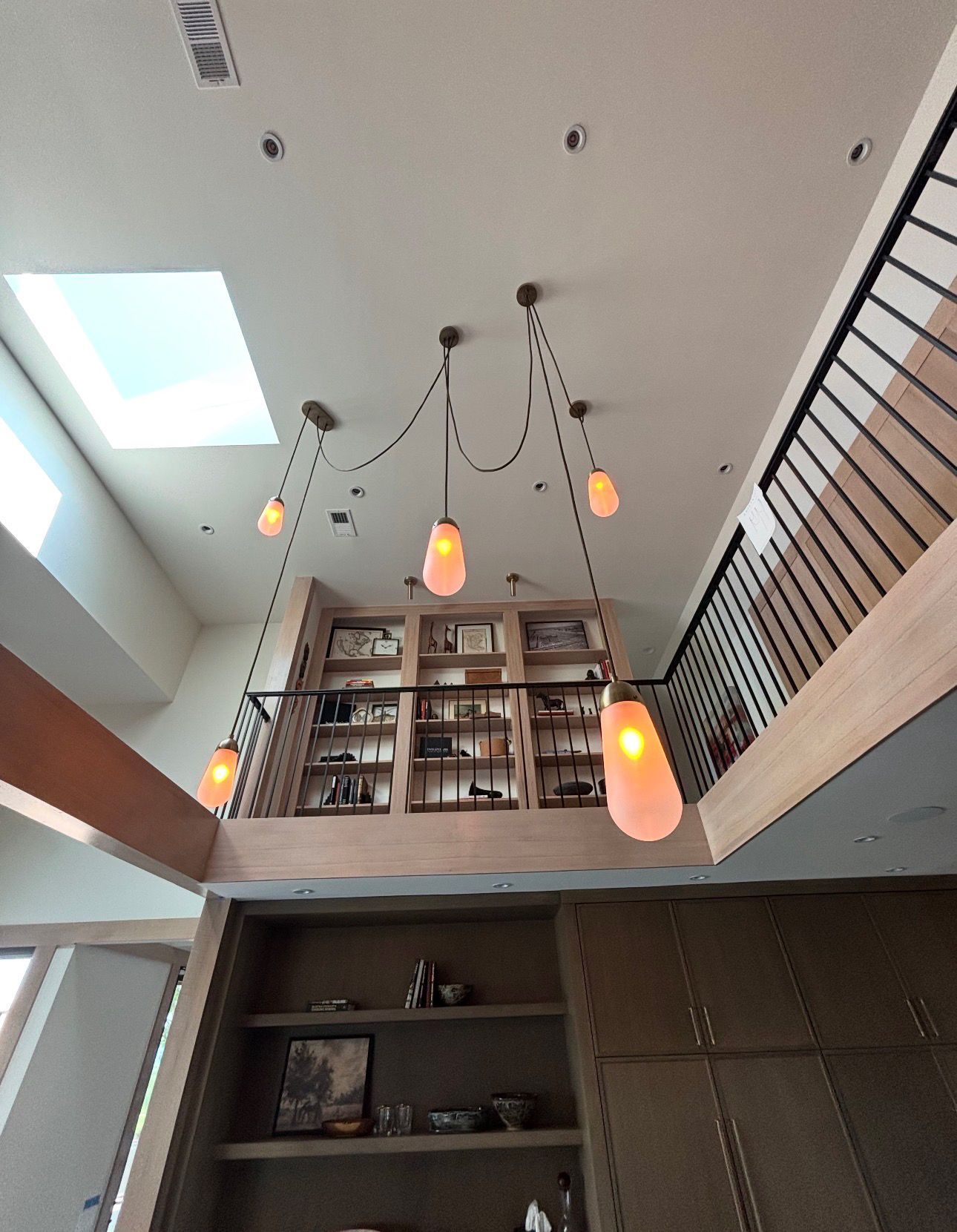 Tall interior with hanging pendant lights, a skylight, and built-in bookshelves above a mezzanine.