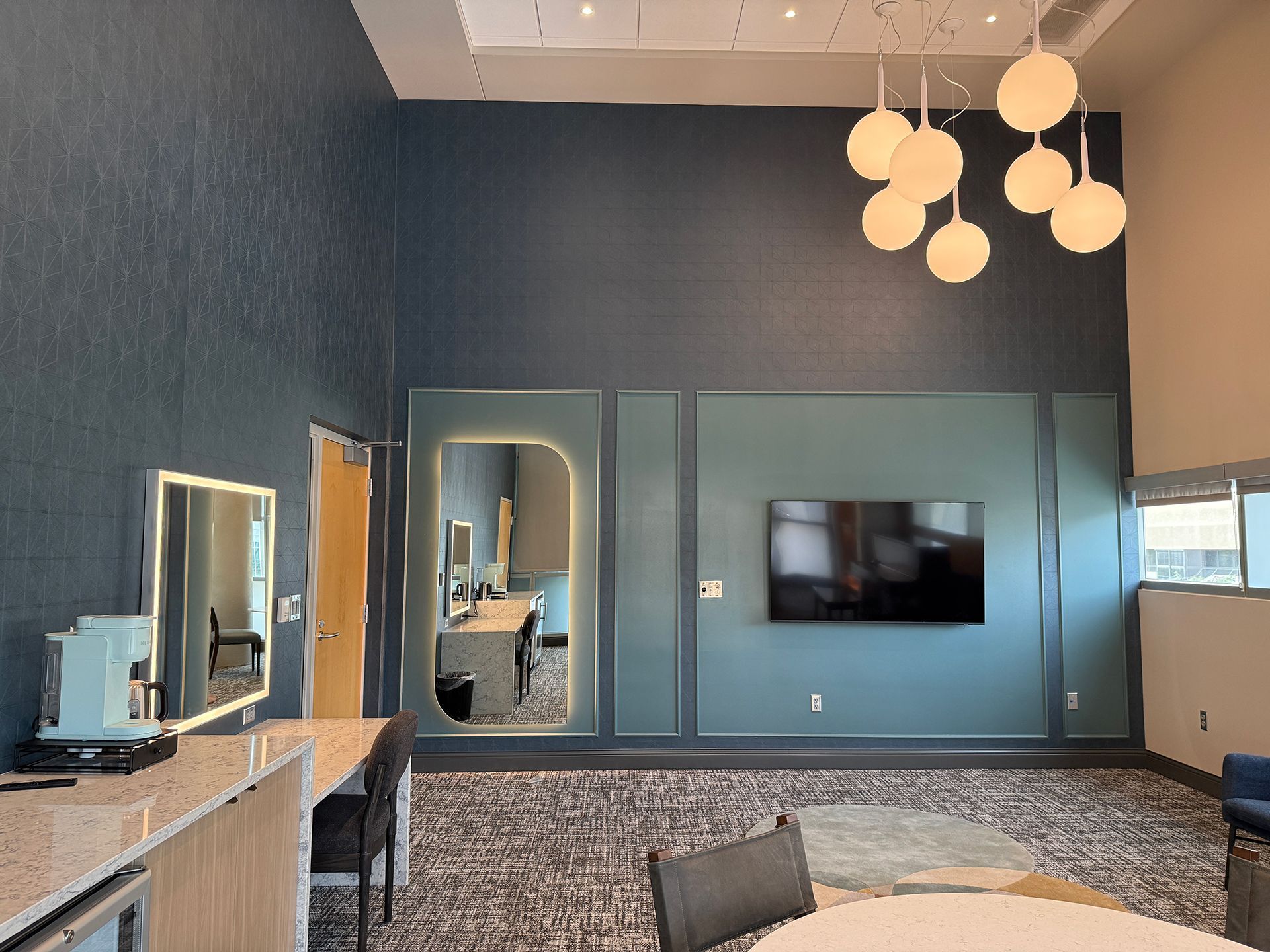 Modern lounge with blue walls, large wall-mounted TV, mirrored doors, and hanging globe lights.