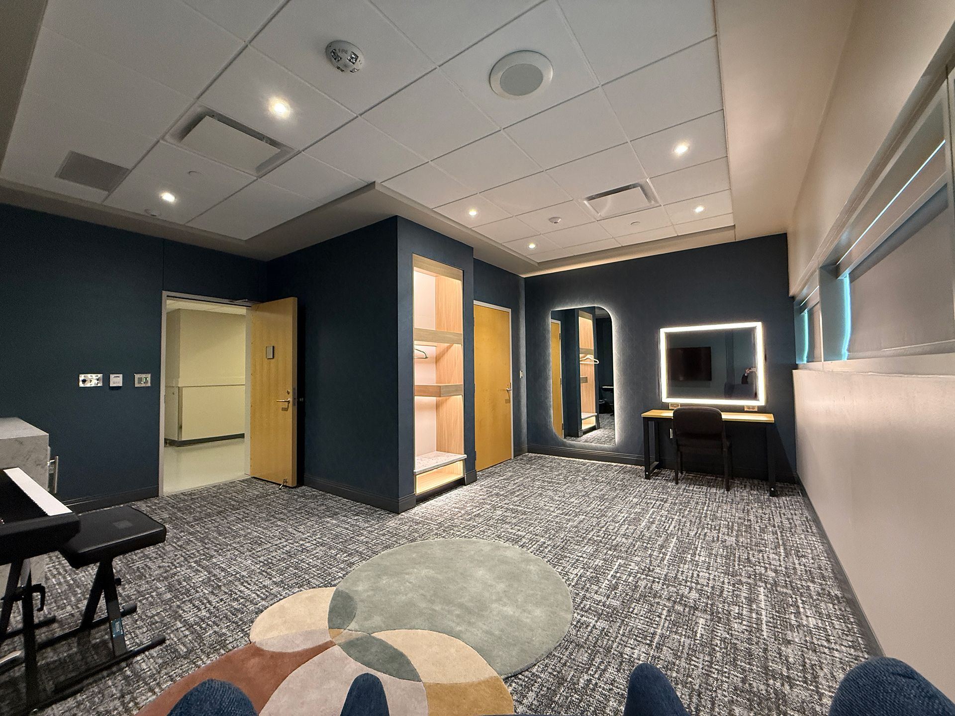 Modern lounge with patterned carpet, dark walls, a desk, chairs, and a lit doorway in a sleek interior.