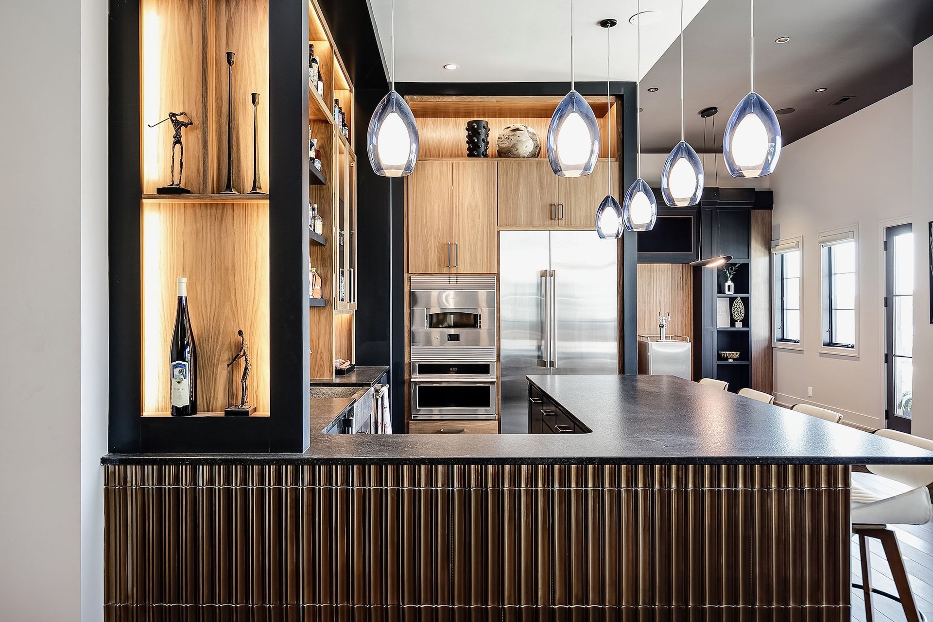 Modern kitchen with wooden cabinetry, pendant lights, granite island, and a dark slatted front counter.