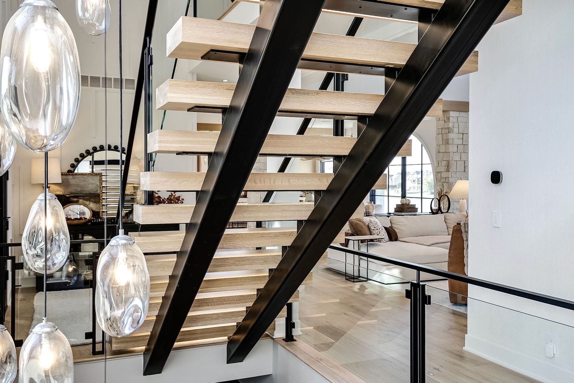 Modern staircase with black steel beams, floating wooden steps, and hanging glass pendant lights in a bright interior