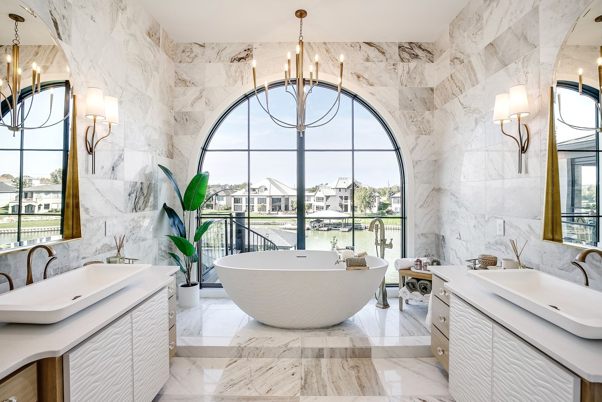 Luxurious white marble bathroom with a freestanding tub and large arched window overlooking a waterfront view