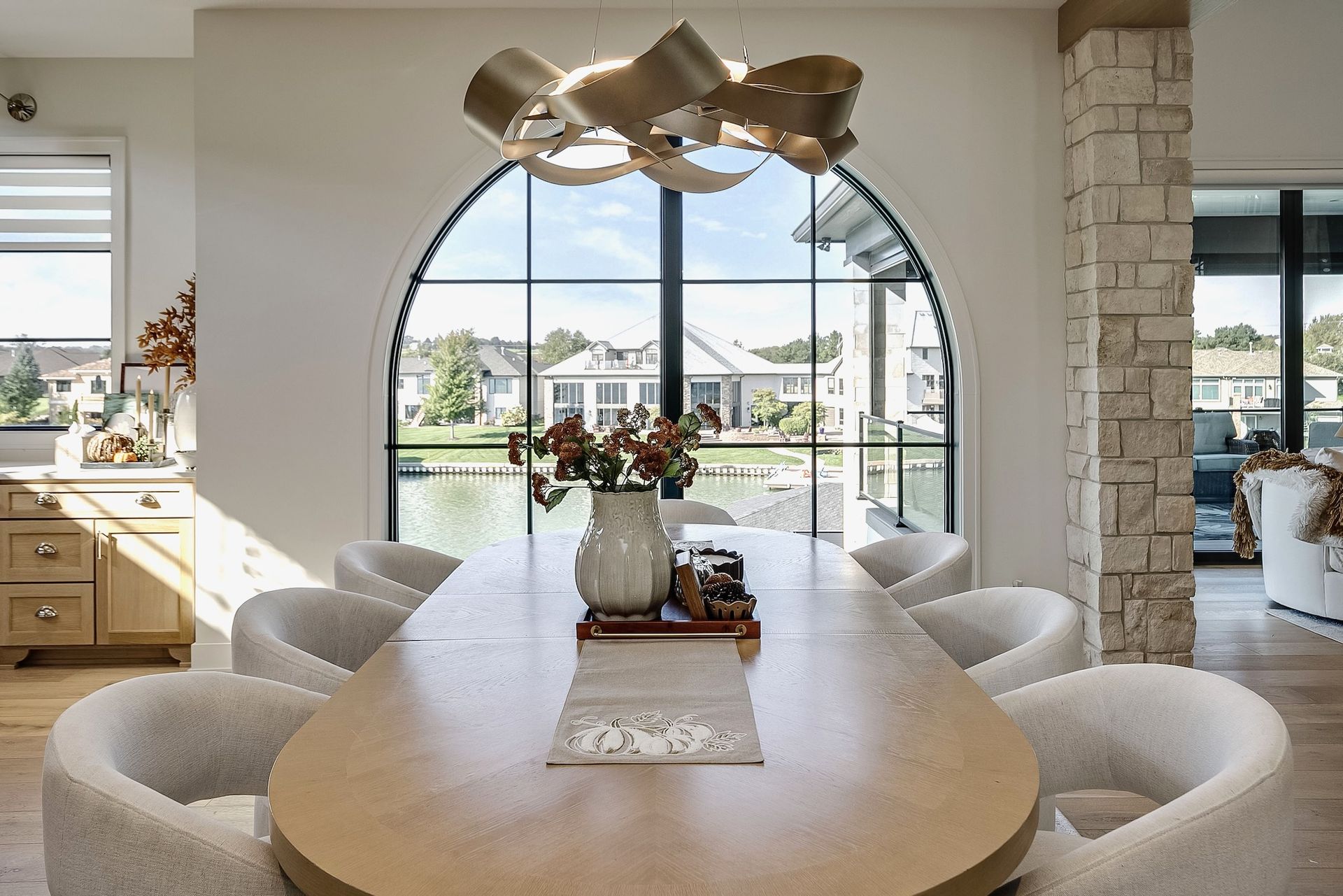 Bright dining room with oval table, curved chairs, and large arched window overlooking mountains.