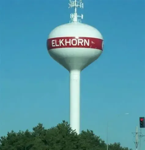 Elkhorn water tower with a red band against a blue sky above trees