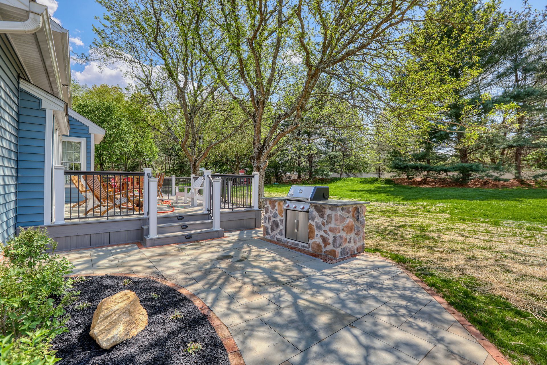 Stone patio with a dining set, built-in grill, pergola, and landscaped garden.