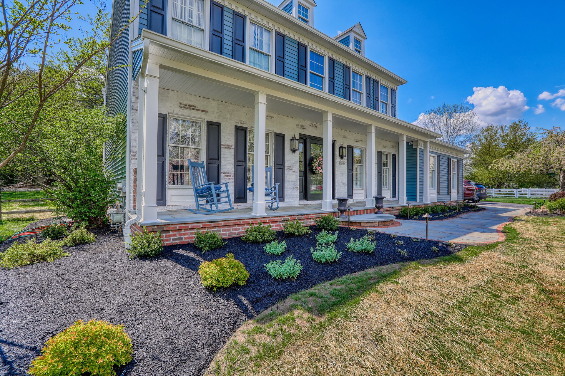 Pool with rock surround, black fence, and colorful flowerbeds on a hillside.