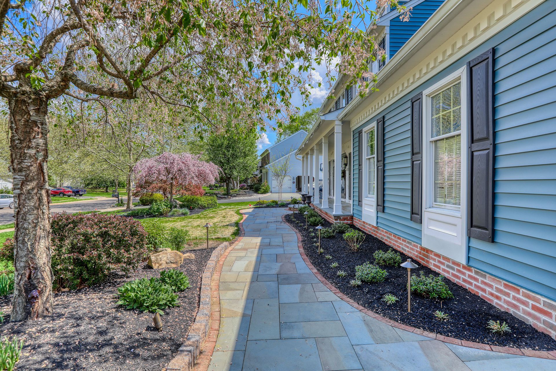 Stone patio with a dining set, built-in grill, pergola, and landscaped garden.