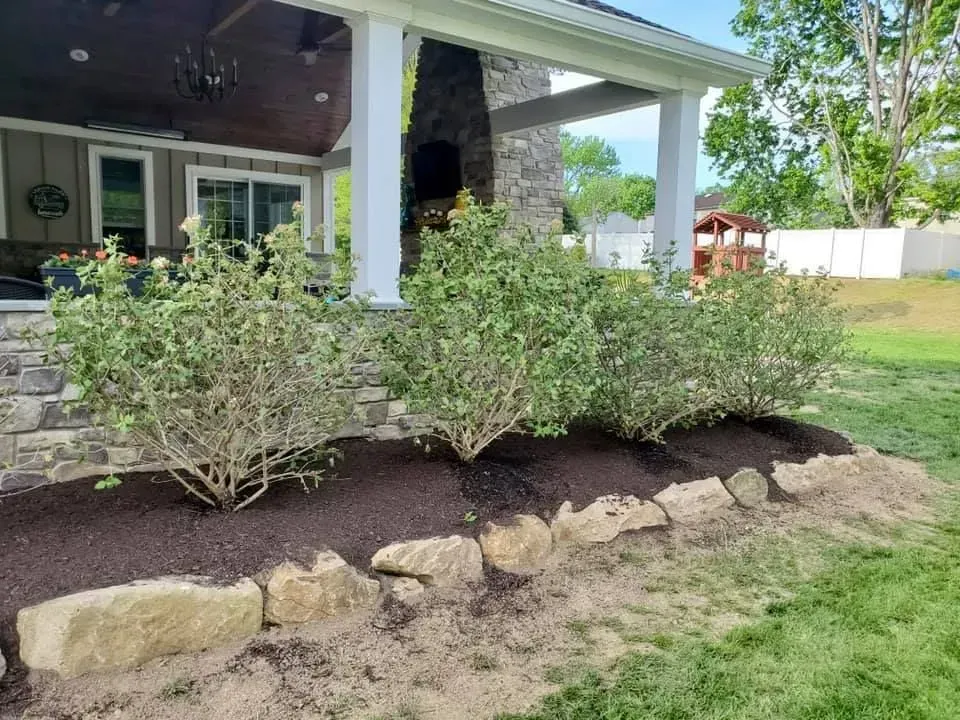 Landscaped yard with bushes, a stone border, and a porch with white columns.
