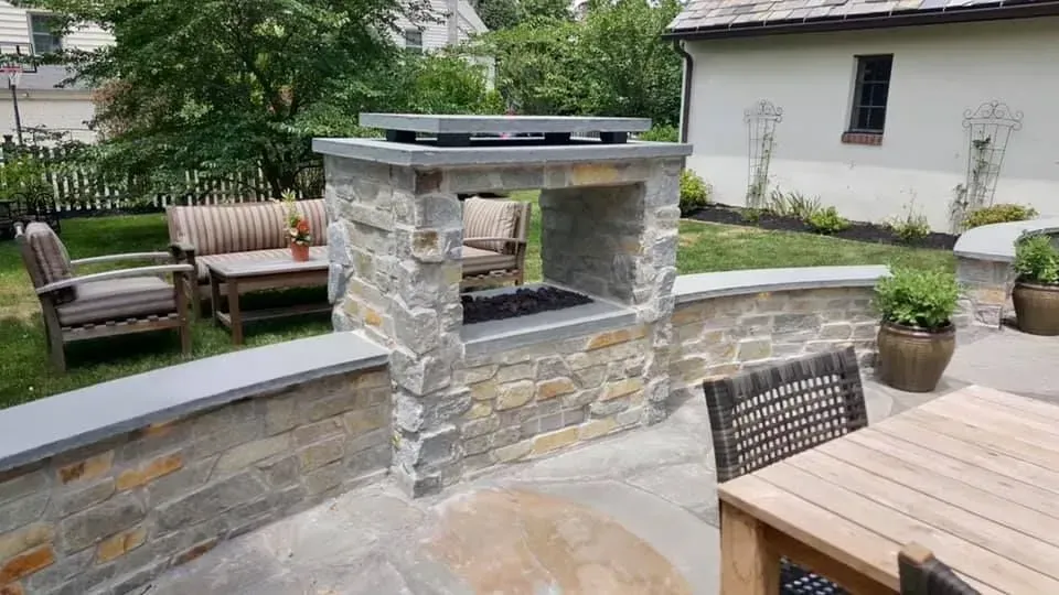 Stone outdoor kitchen with grill, seating area, and lush green lawn.
