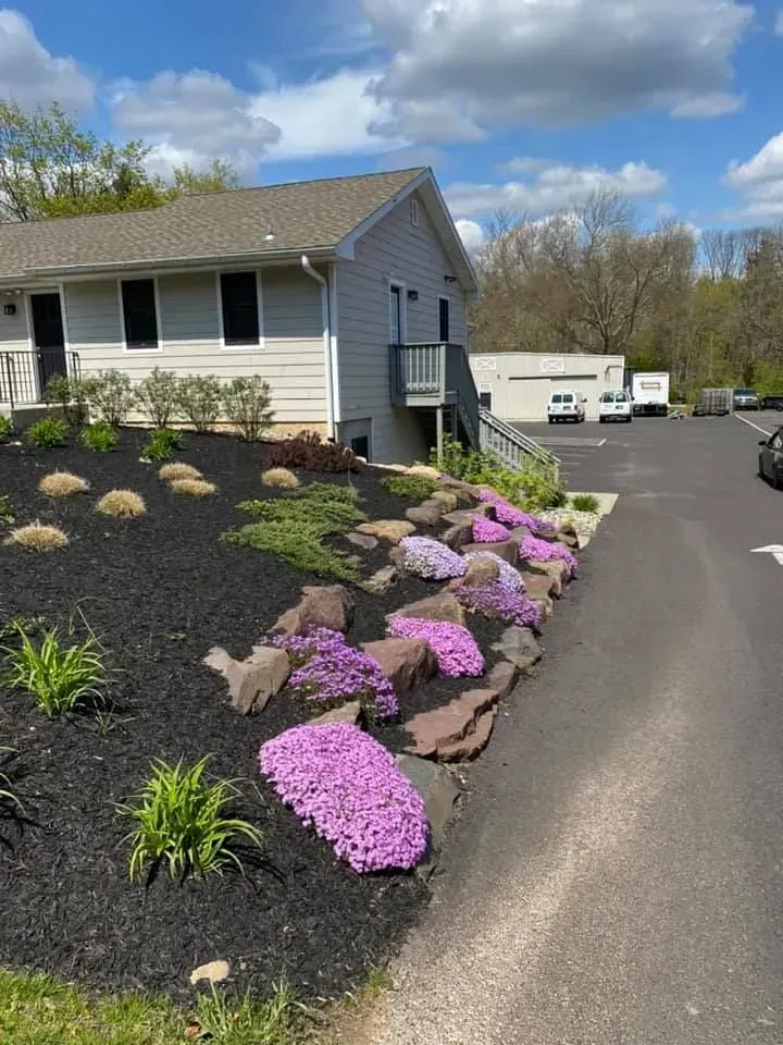 Exterior of a light gray building with a landscaped garden featuring purple flowers and black mulch.