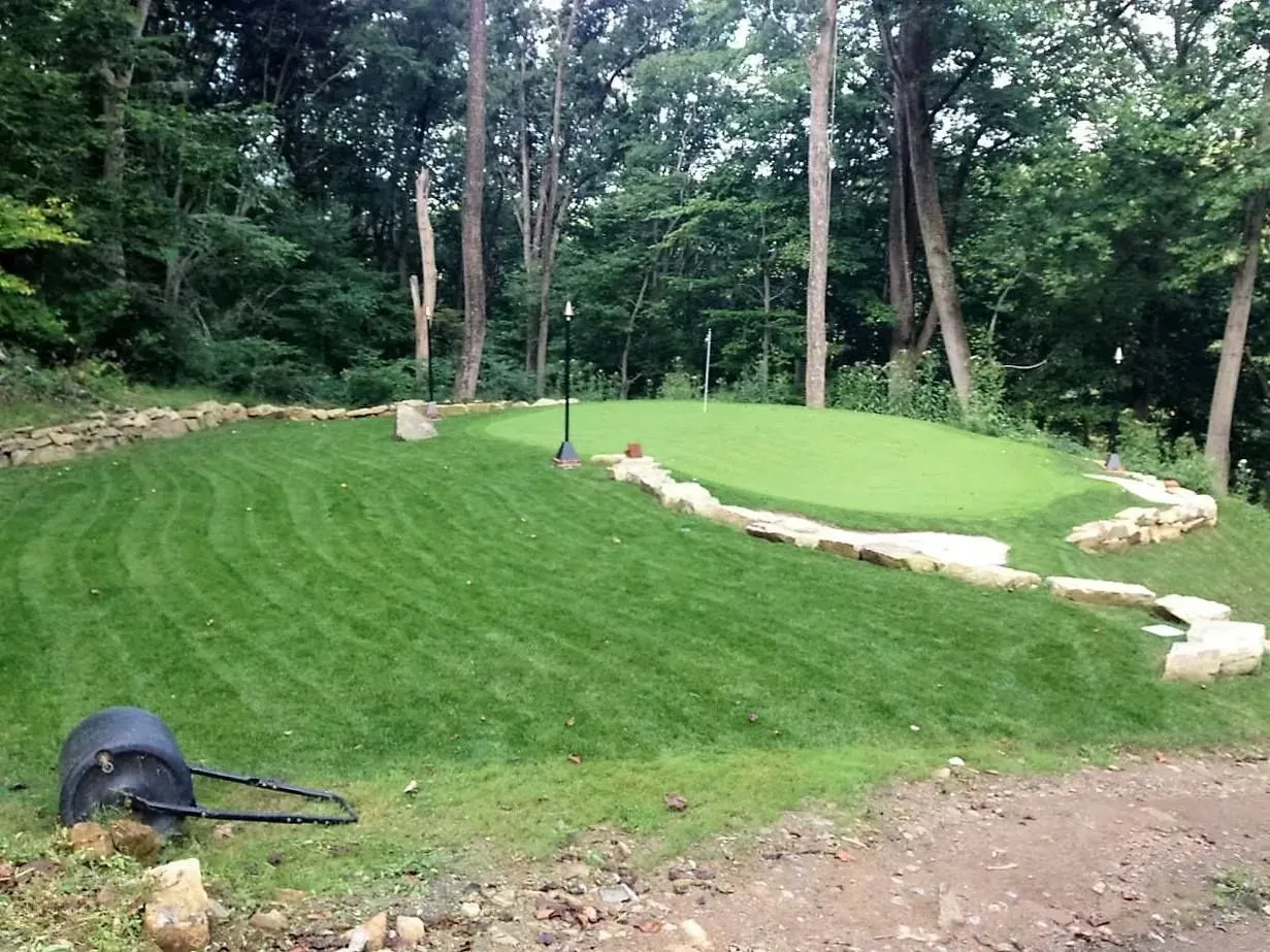 Green golf putting green with stone border surrounded by trees.