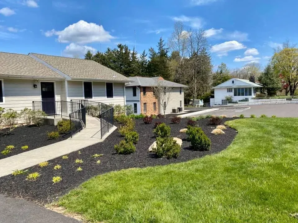Exterior view of multi-unit buildings with landscaping; green lawn, black mulch, blue sky.