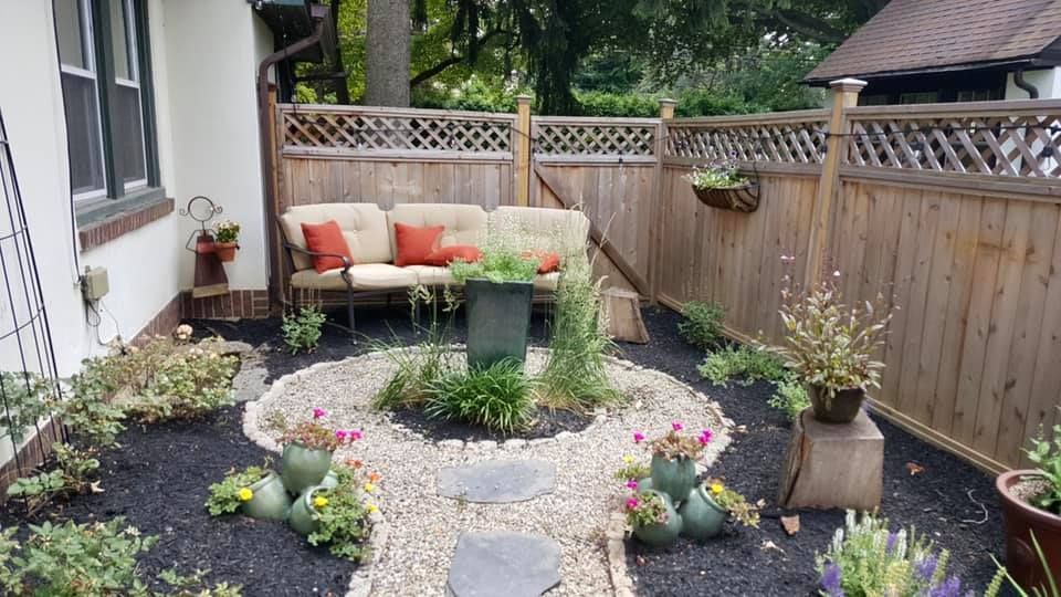 Cozy backyard seating area with stone path, fountain, flower pots, and wooden fence.