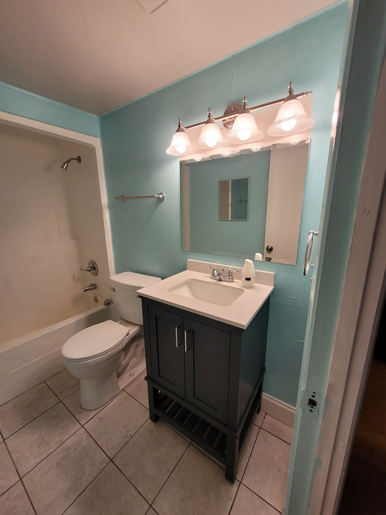 Blue bathroom with vanity, toilet, and bathtub. White tile floor, light fixtures.