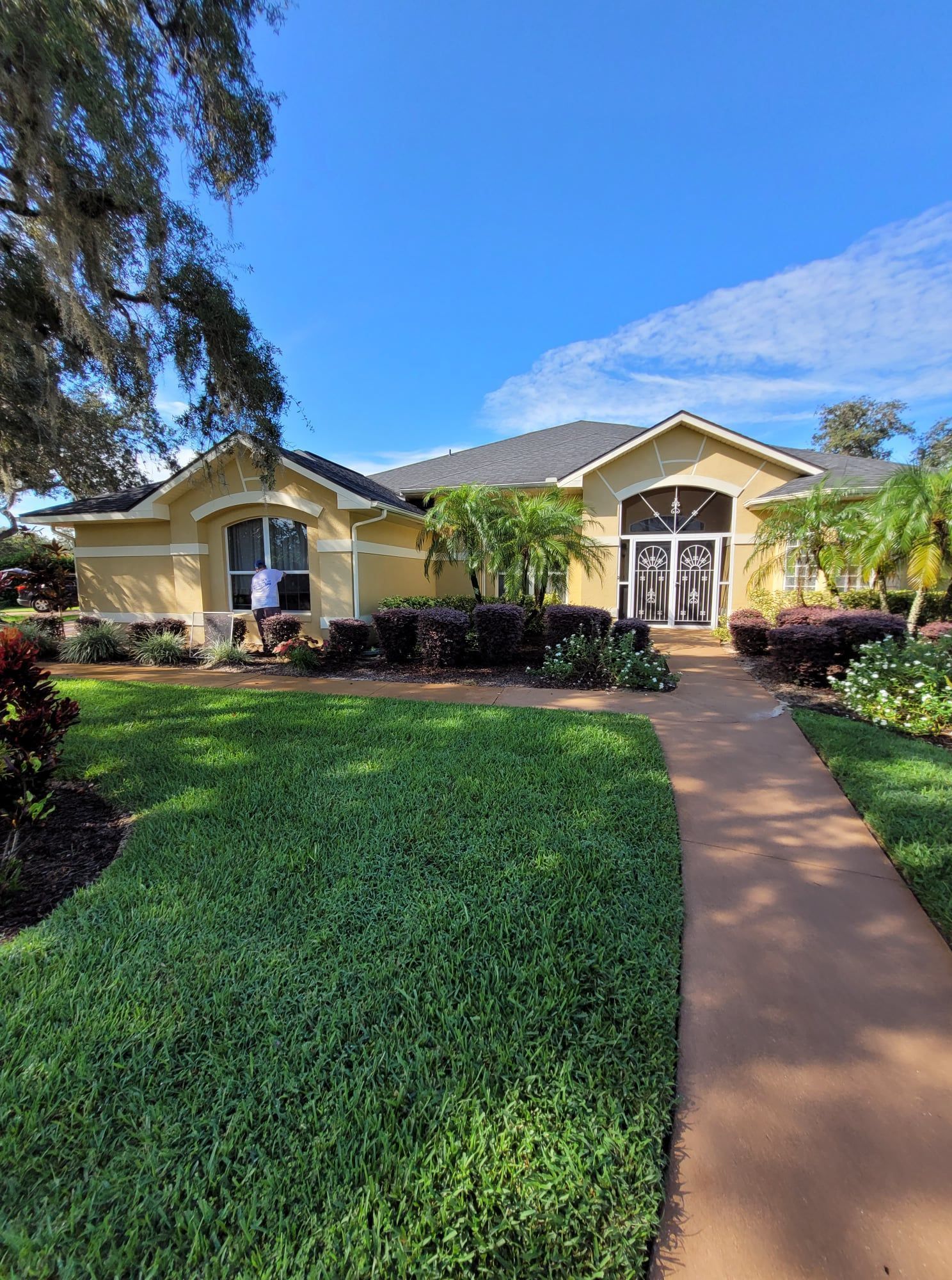 Yellow house with brown walkway and green lawn under a bright blue sky.