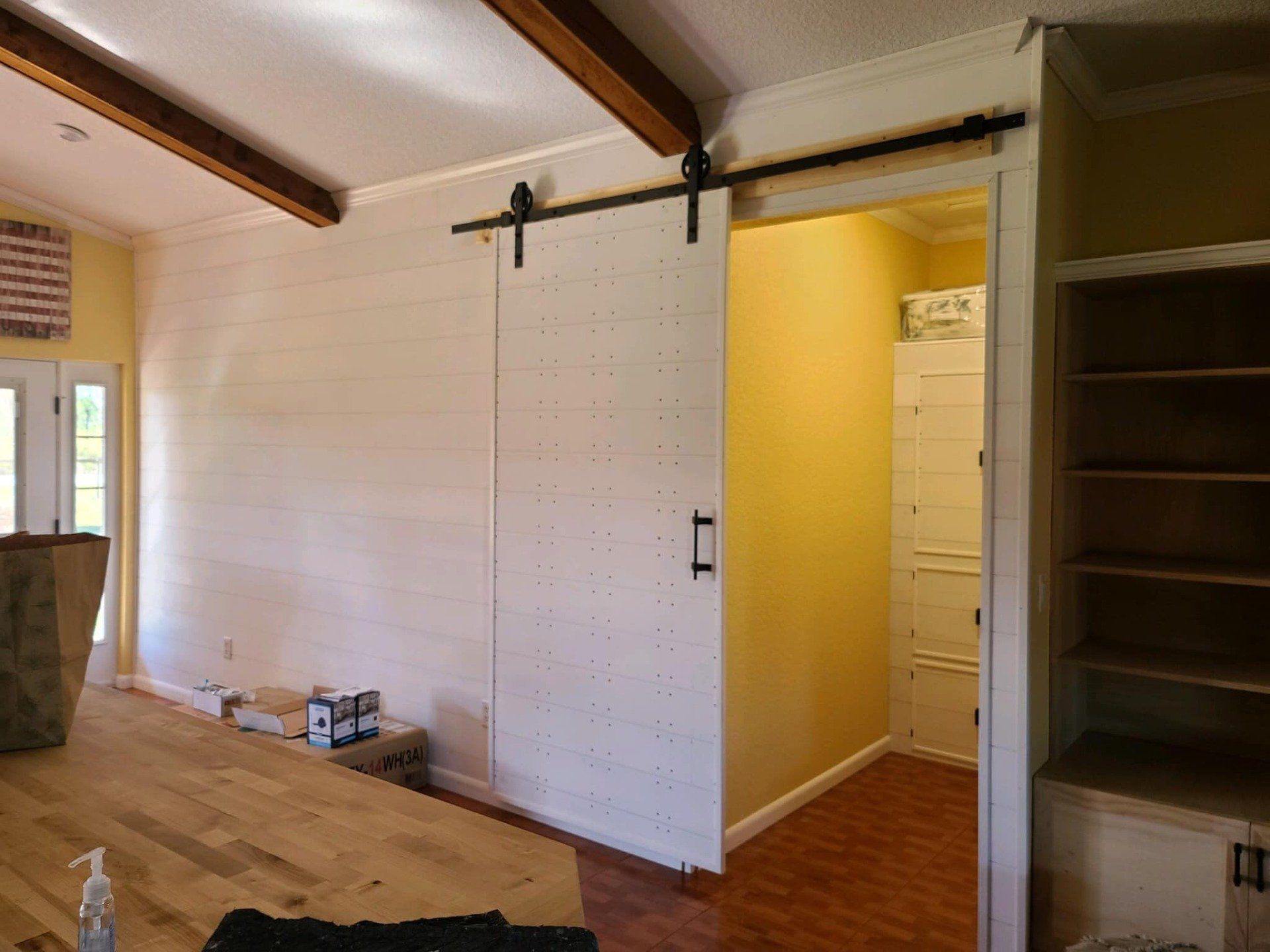 Barn door, white with black hardware, on yellow wall, next to built-in shelves.