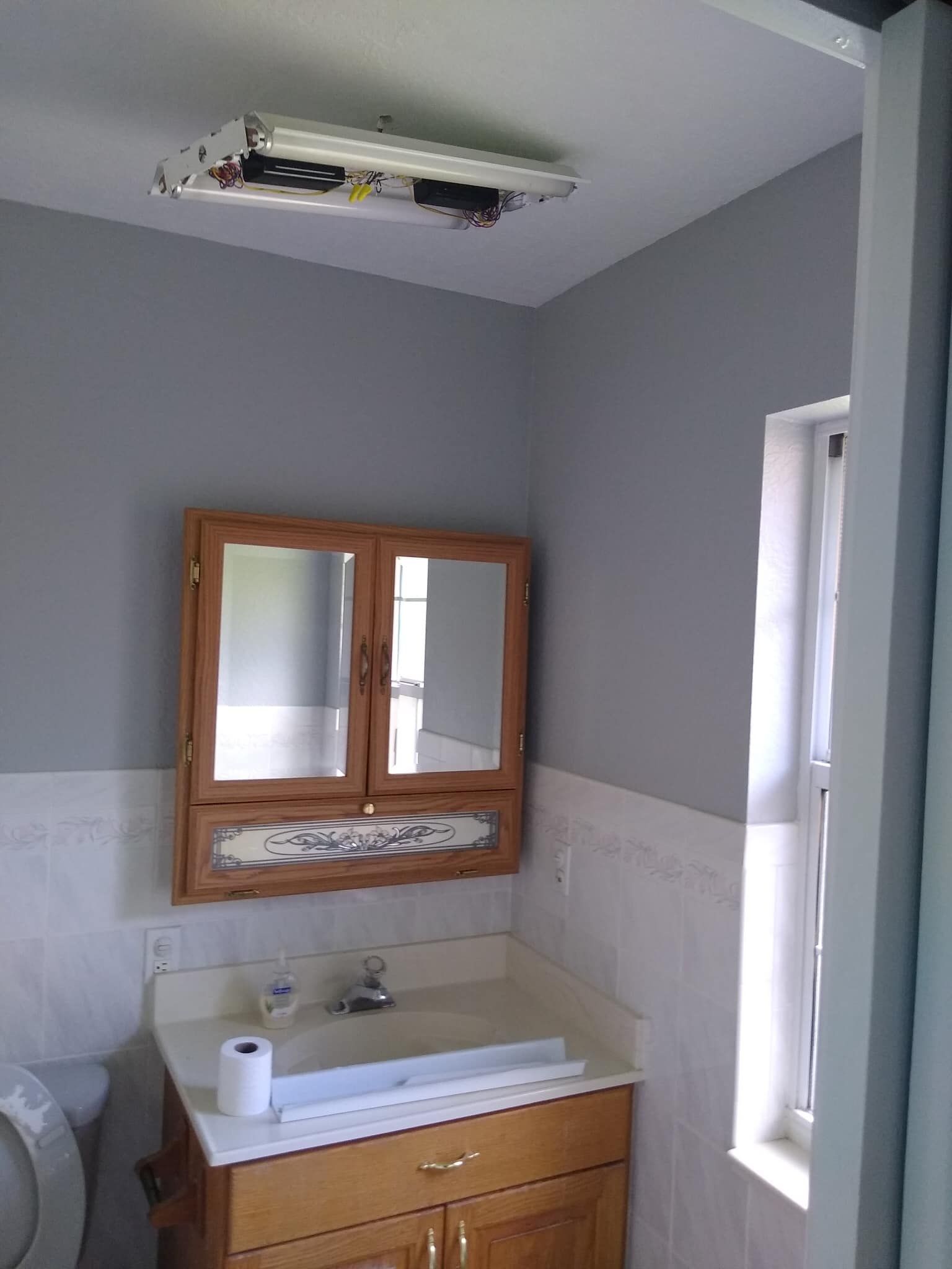 Bathroom with gray walls, wood vanity, mirrored medicine cabinet, and a window.
