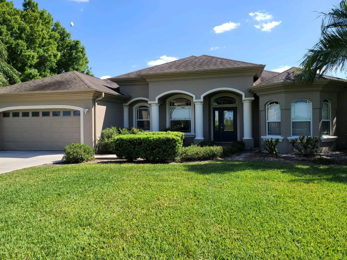 Tan stucco house with a dark door, arched windows, and a green lawn under a blue sky.