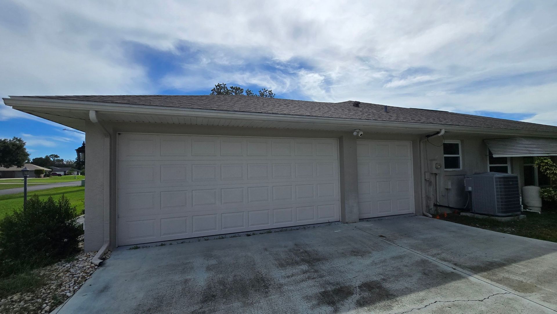 Two-car garage with two white doors, light gray trim, and a tiled roof, under a cloudy sky.