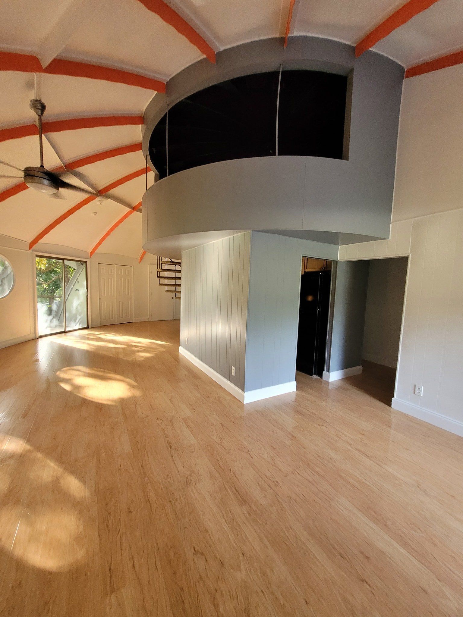 Spacious interior with curved ceiling, balcony, and light-colored flooring. Natural light streams in.