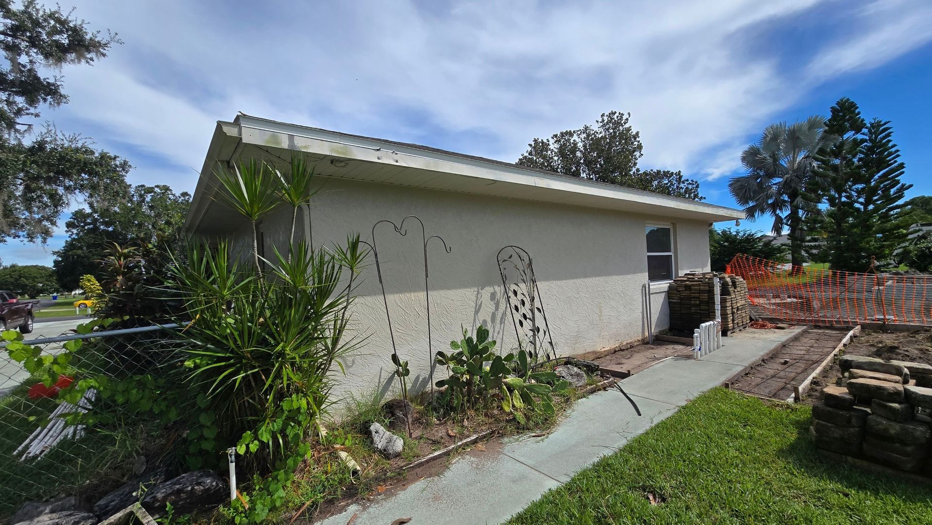 Beige stucco building with a slanted roof, a small window, and a concrete path. Landscaping and blue sky.