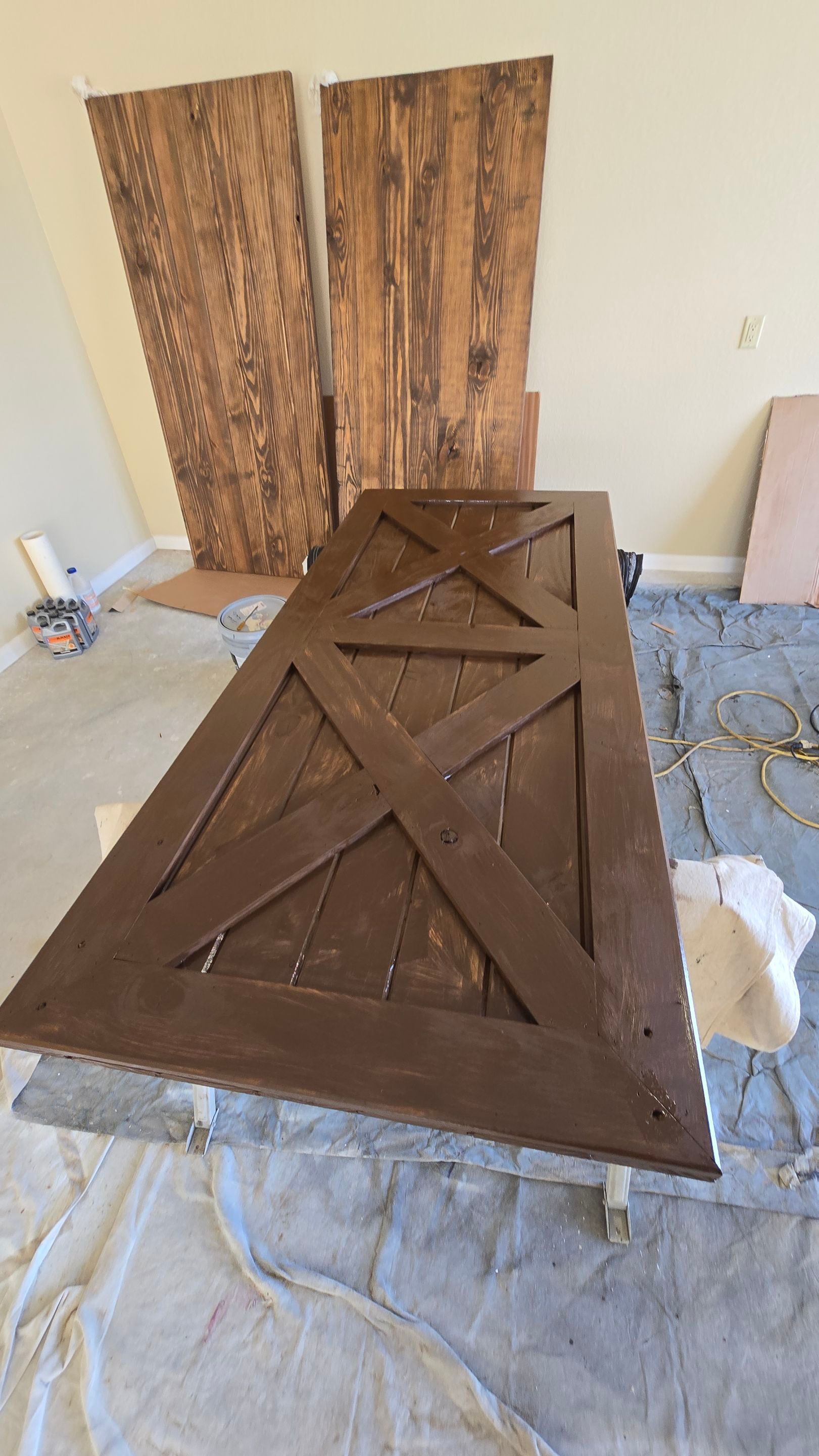 A large, stained wooden door with an X design, leaning against a wall. More stained planks are visible.