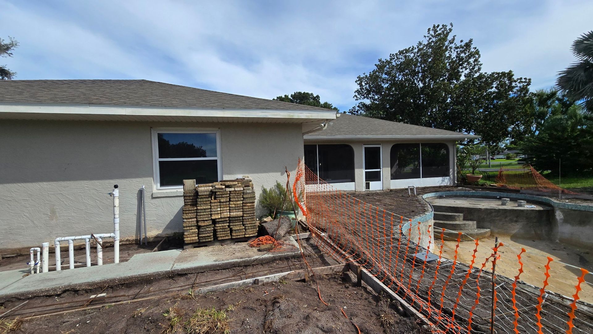 House with a screened-in porch under construction. Orange safety fencing surrounds a raised area.