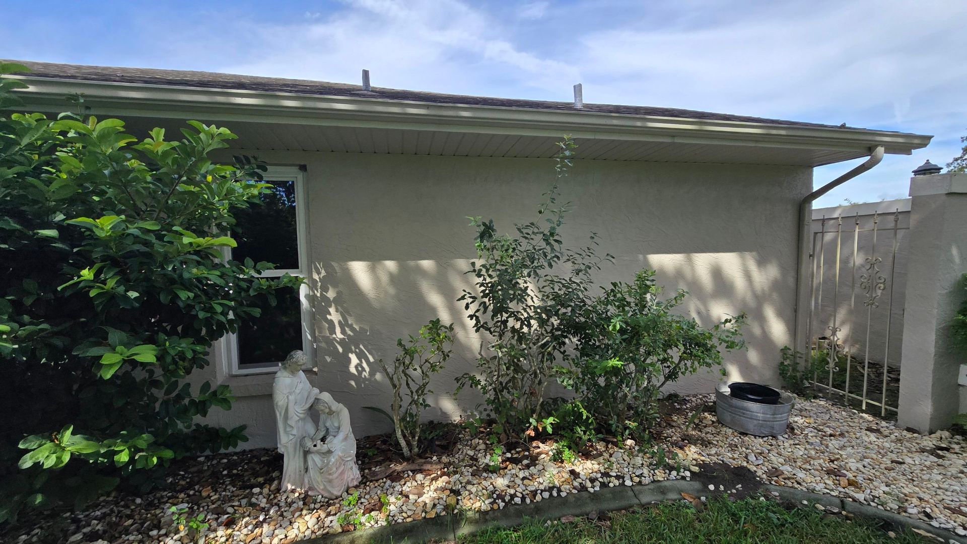 Beige stucco building with a window and shrubs in a garden bed with rocks.