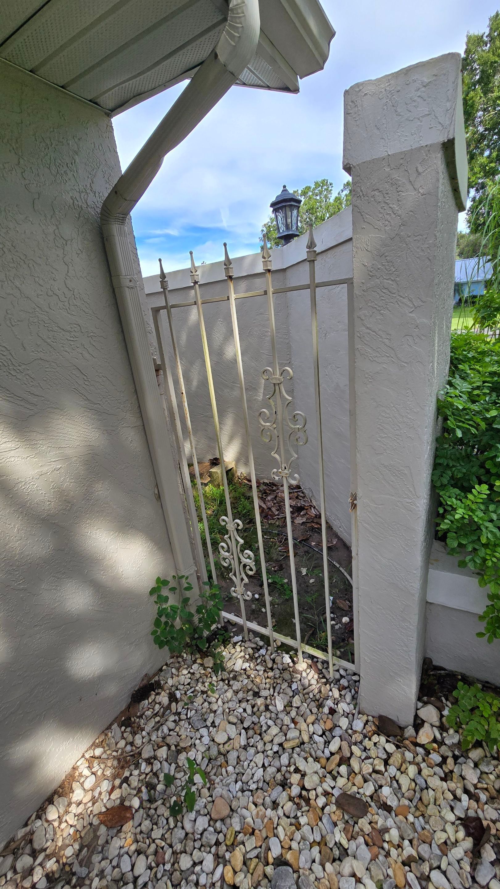 Wrought iron gate set in a stucco wall, gravel pathway. Overcast sky visible above.