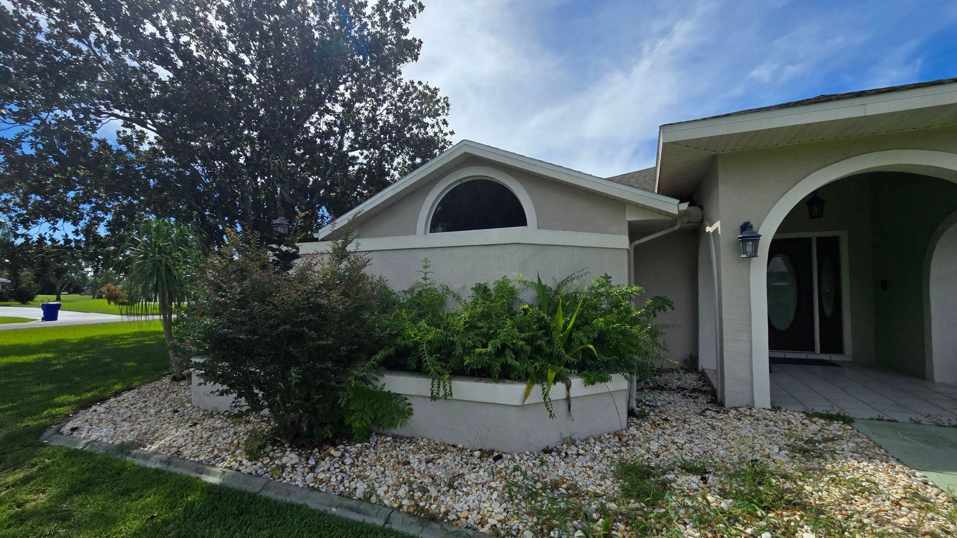 A beige house exterior with shrubs, a curved window, and a blue sky.