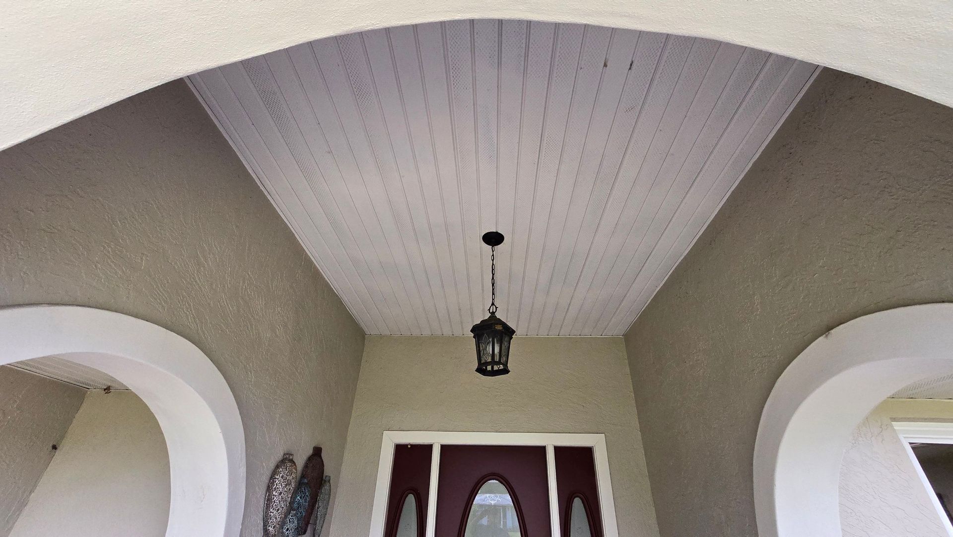 Covered entry porch with arched ceiling, light fixture, and front door.