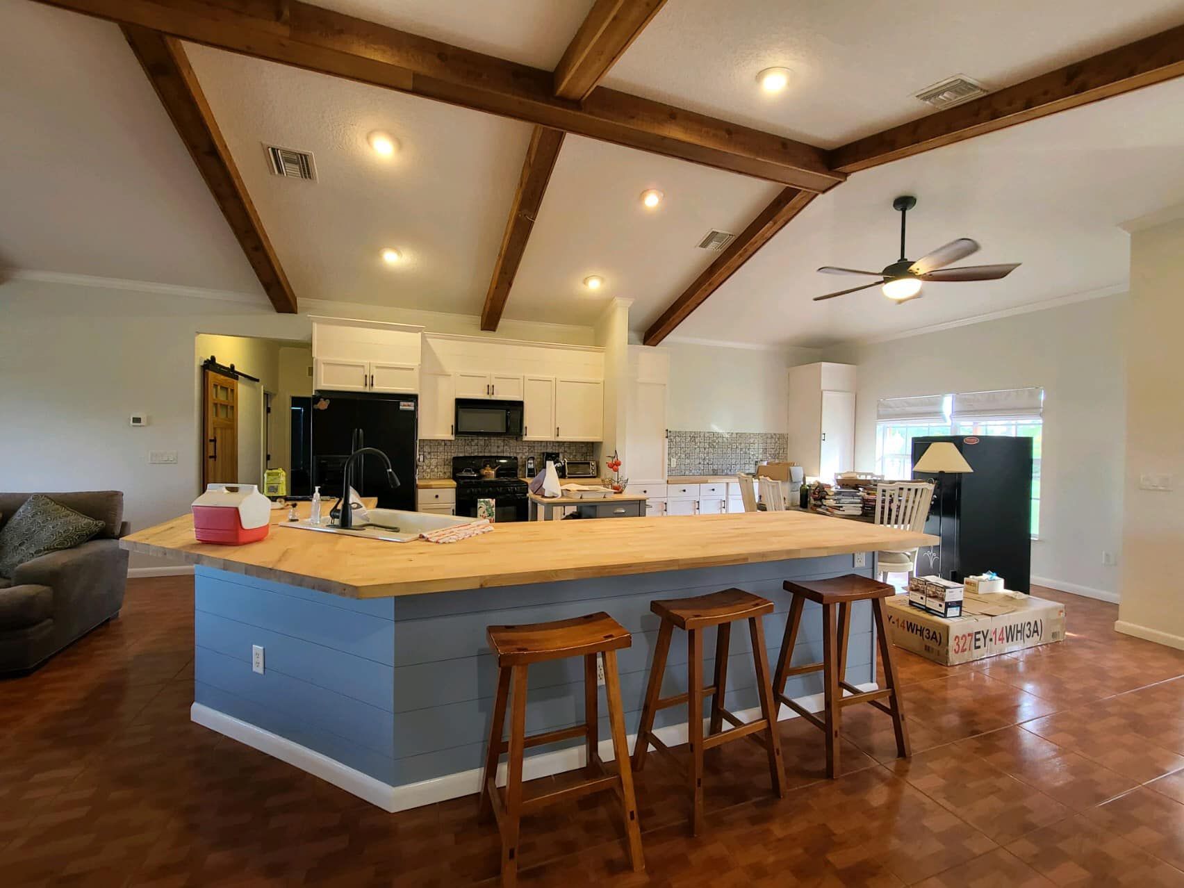 Kitchen with island, light wood ceiling beams, white cabinets, blue island base, and wood stools.