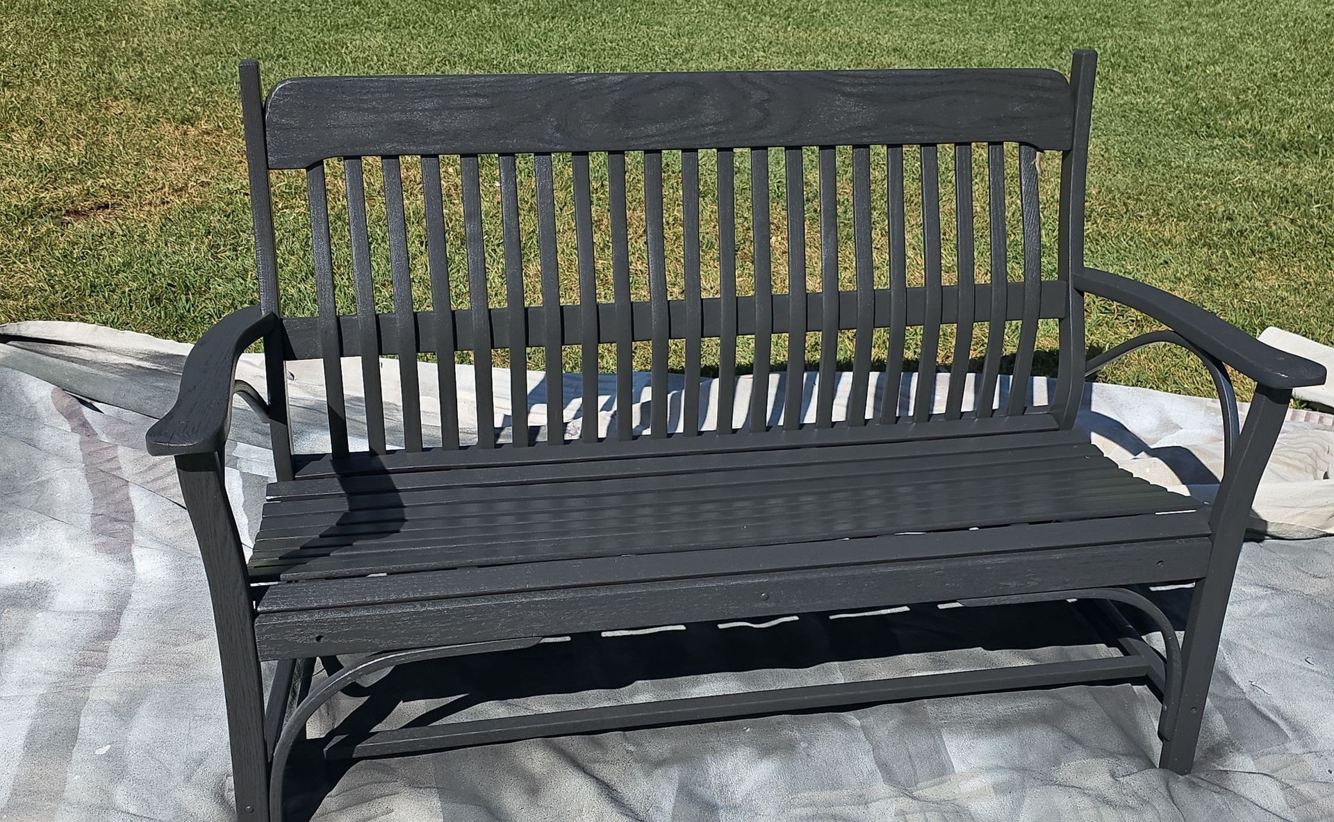 Dark gray wooden outdoor bench on a concrete surface, with a grassy background.