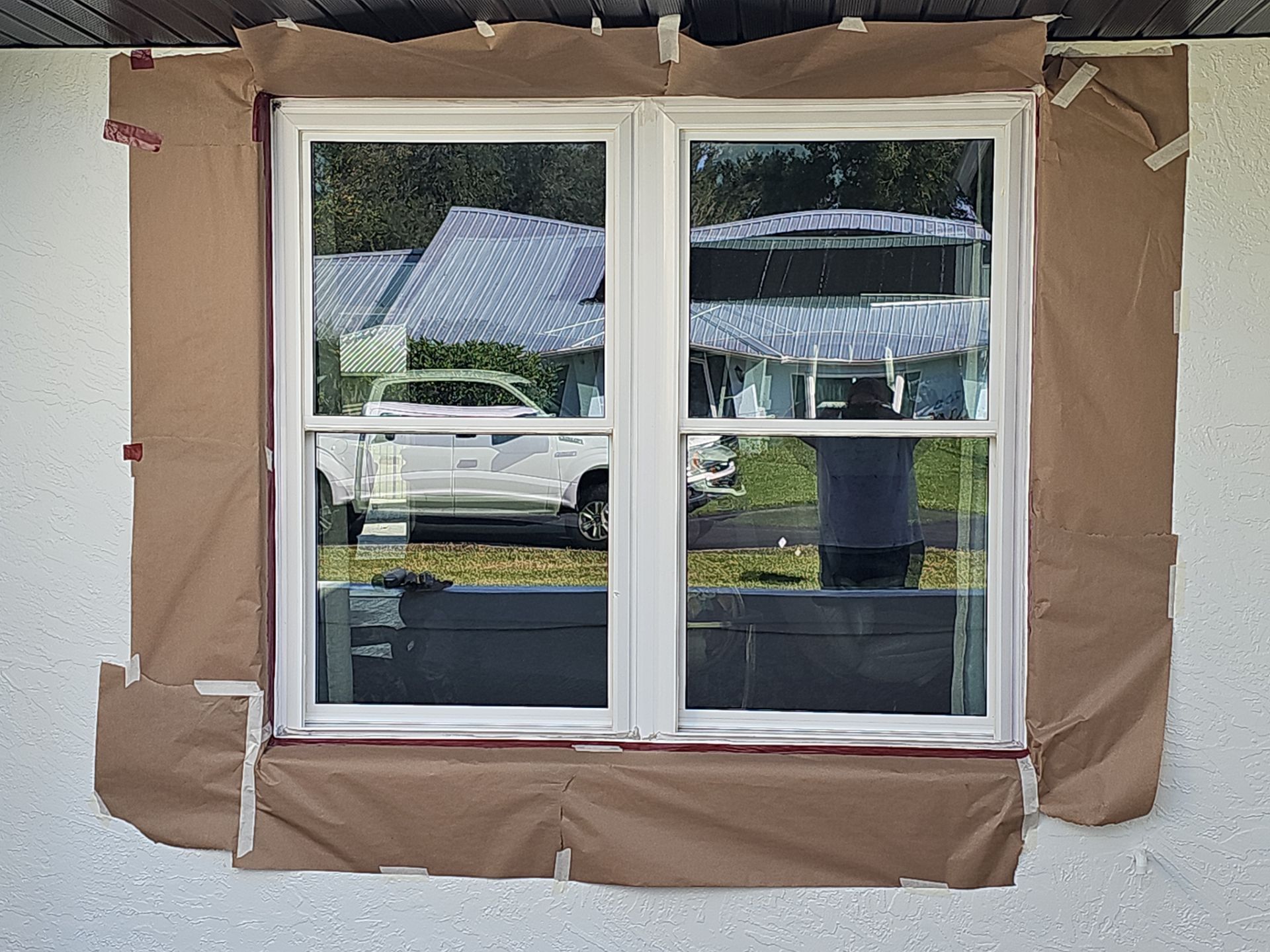 Window covered in brown paper for painting, with white frame, and a reflection of a truck.
