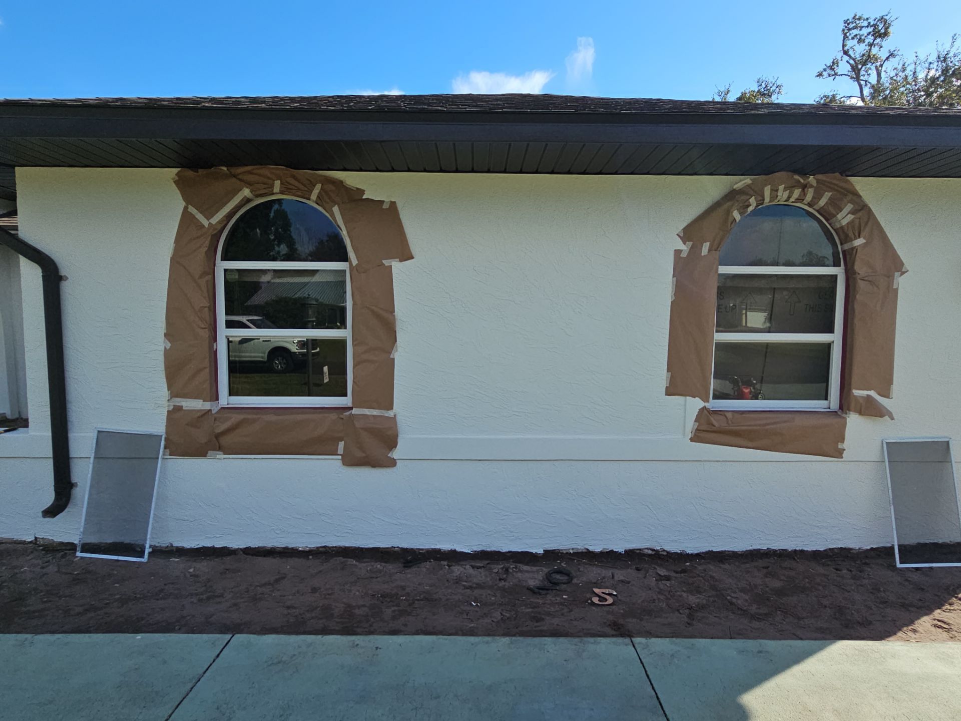 Exterior wall with two arched windows, taped for painting. White stucco, brown tape. Sunny day.