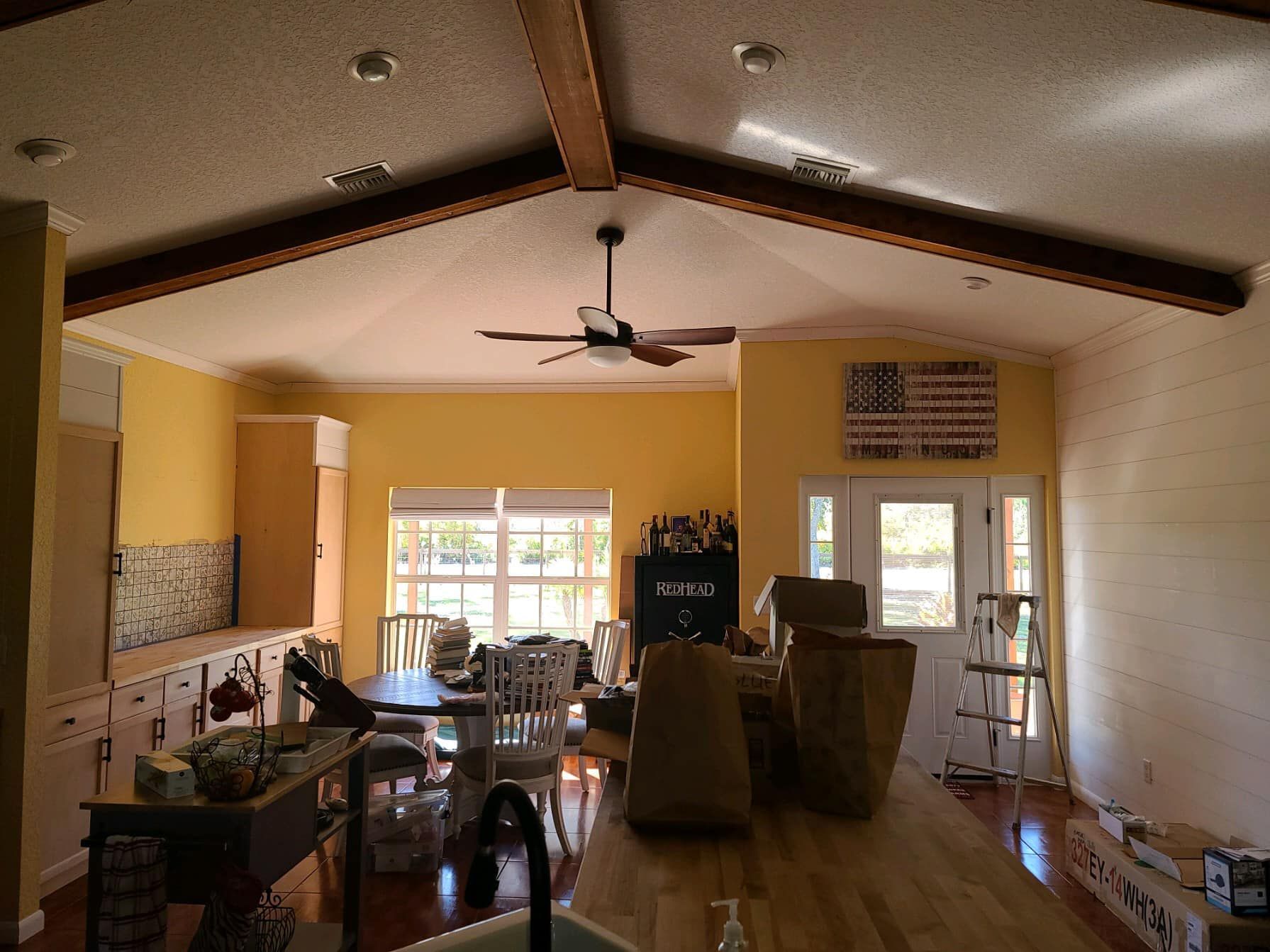 Interior kitchen with wood beams, yellow walls, and a ceiling fan. An American flag hangs on the wall.