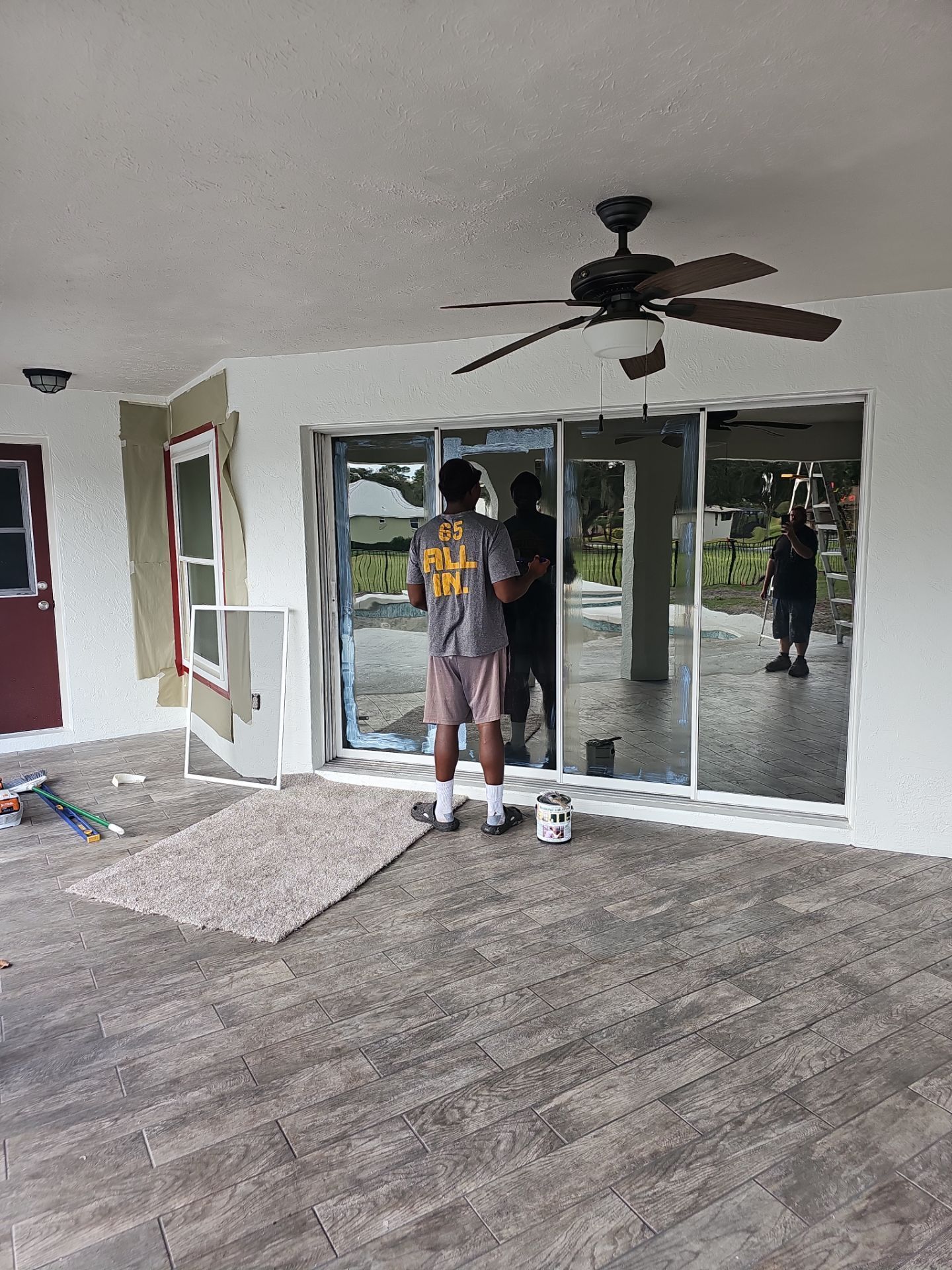 Man standing in front of sliding glass doors. Patio with a ceiling fan.