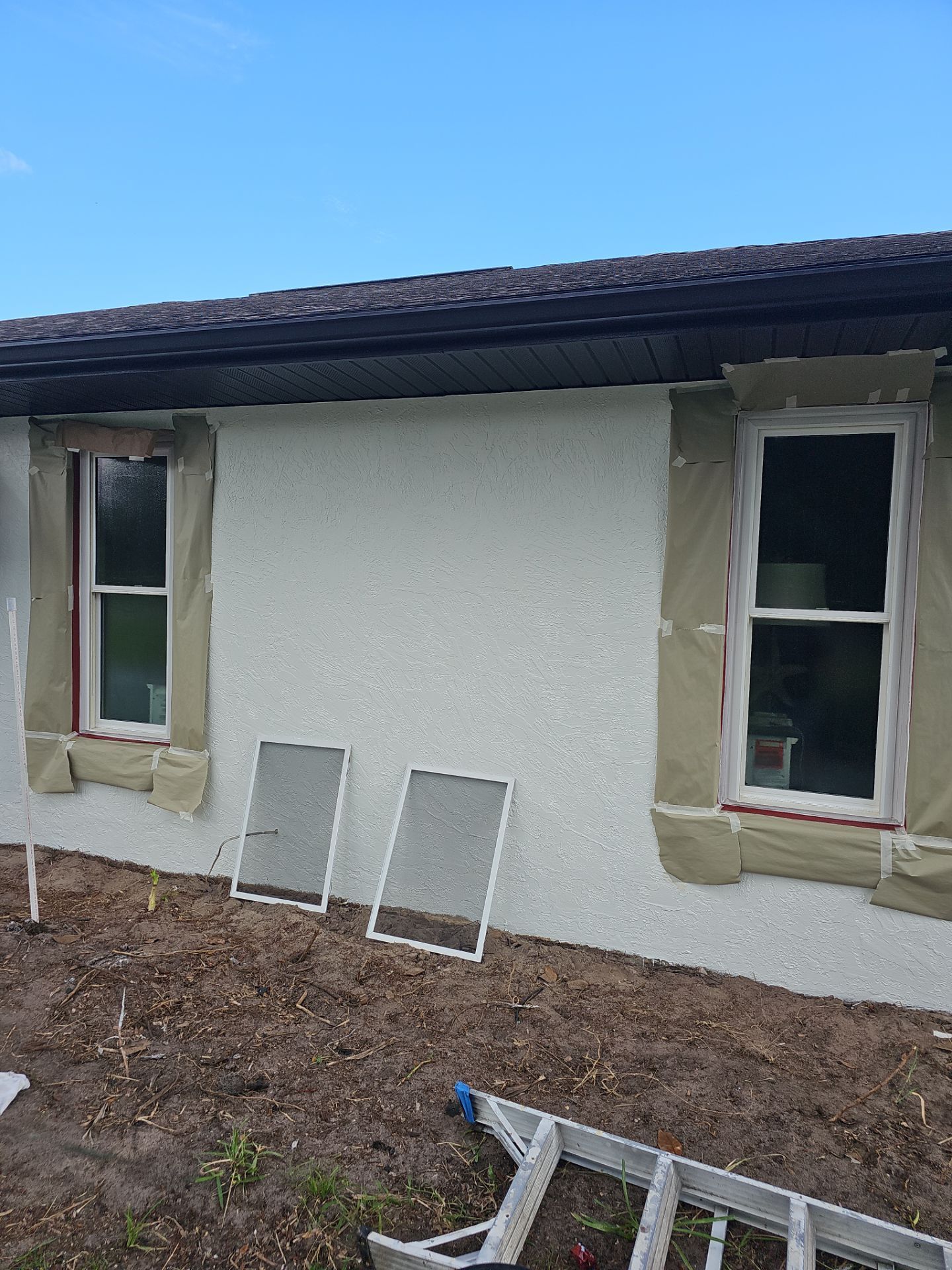 Exterior wall with two windows and insulation, two window screens, ladder, and a blue sky.