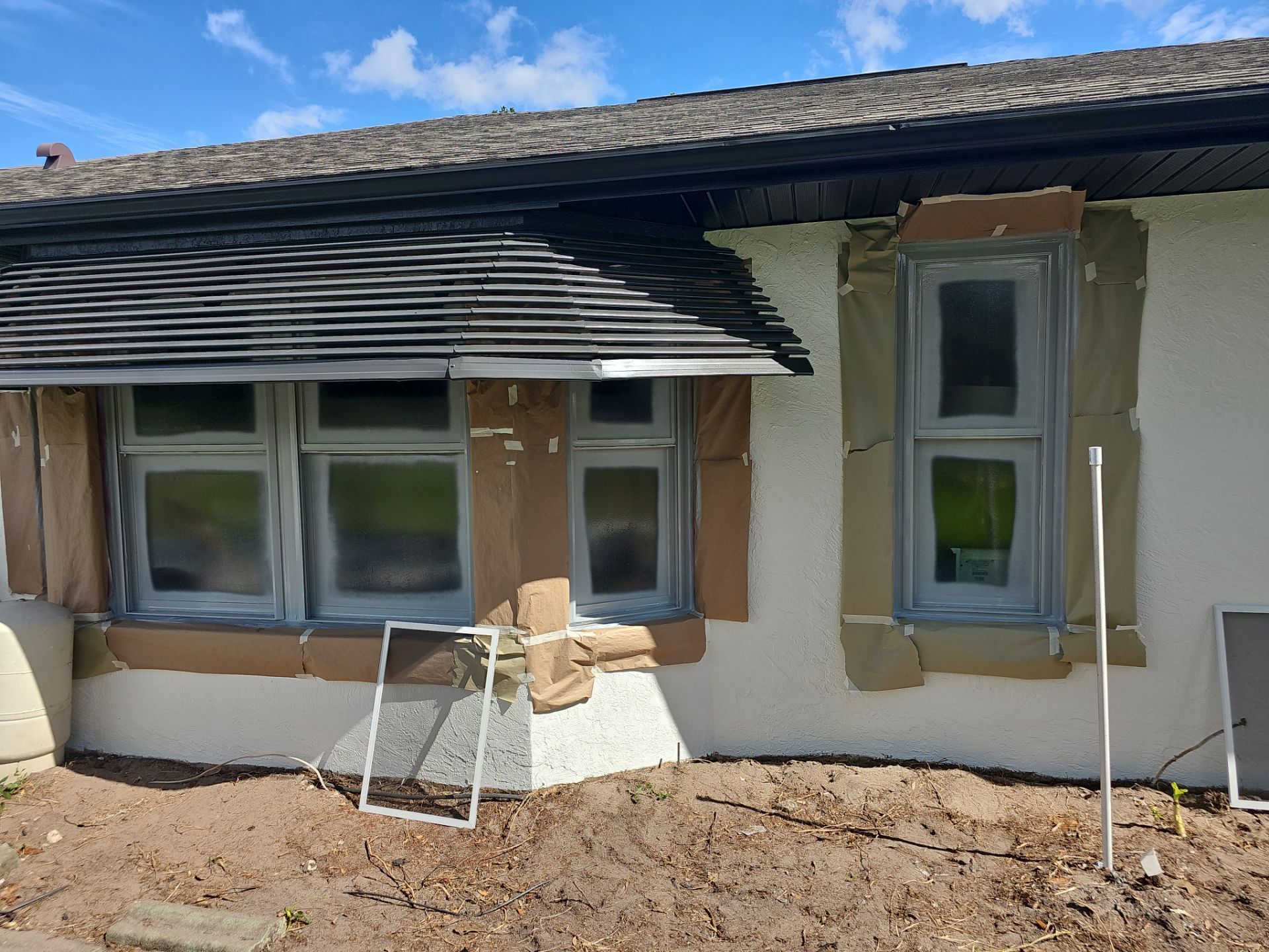 Exterior of a white house with windows taped for painting. Brown cardboard covers window frames.