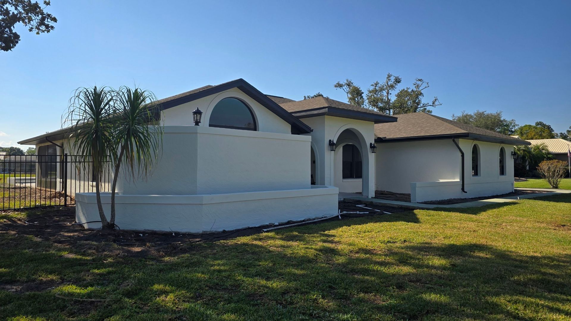 White stucco house with dark roof and green lawn on a sunny day.