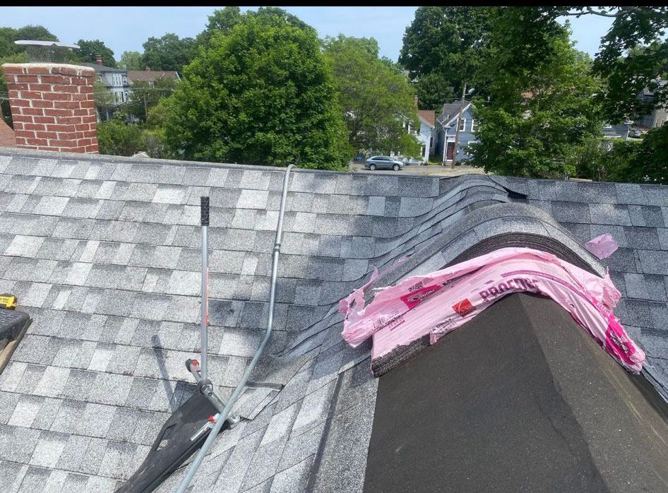 Roofing work in progress on a residential roof, asphalt shingles, insulation exposed.