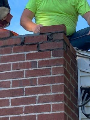 Person in lime green shirt placing a brick on top of a brick chimney.