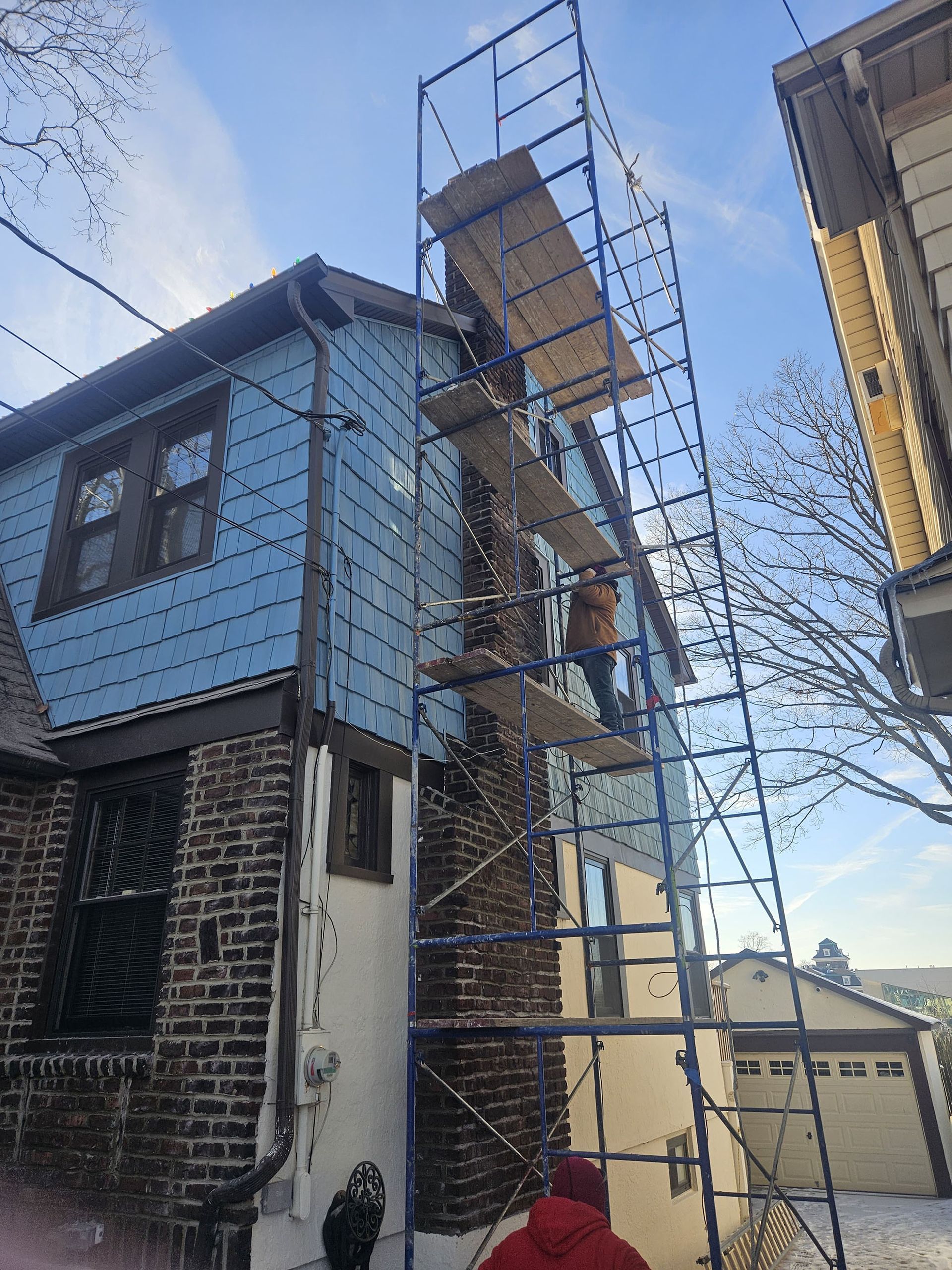 Scaffolding next to a blue house, person on a platform, sunny day.