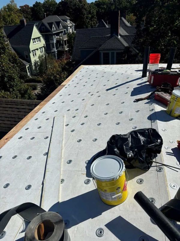 Rooftop under construction; white membrane secured with fasteners, tools and materials visible.