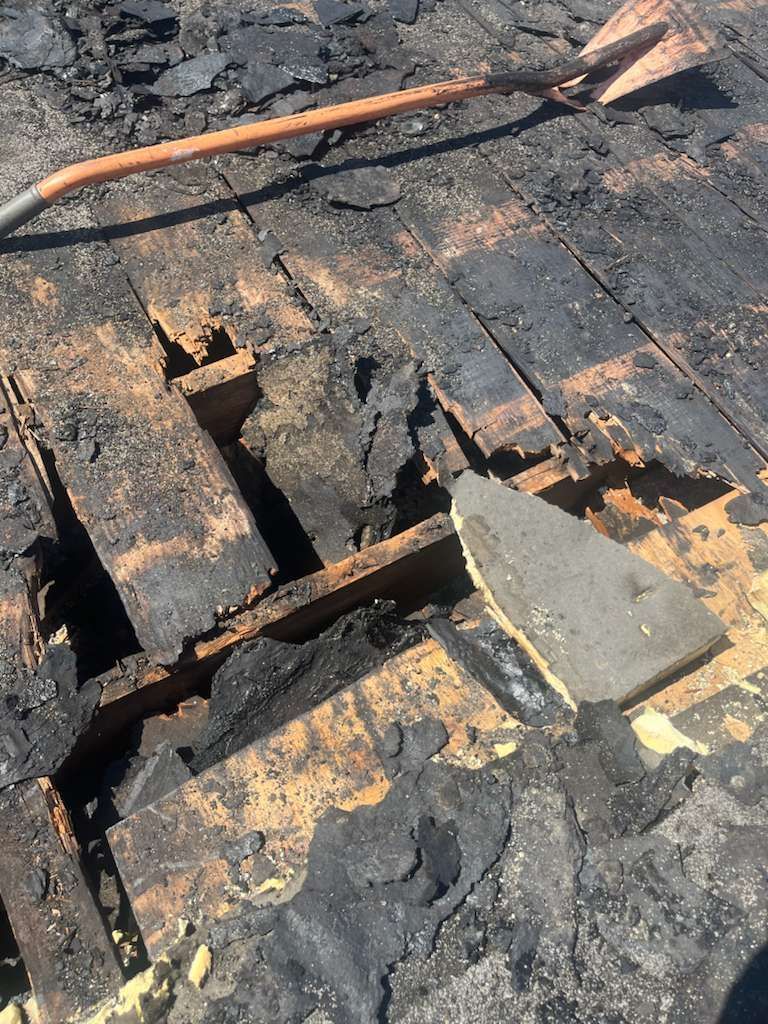 Damaged, charred wooden roof with missing boards and debris. A metal tool rests on top.
